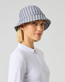 A woman wearing a gray and white vertically striped bucket hat and a white long-sleeve zip-up shirt, photographed against a solid light gray studio background.