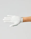 A white leather golf glove with perforated details, worn on a person's hand and arm against a solid light gray background.