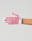 A gardening glove with a red and white gingham pattern and white finger tips, worn on a person's hand against a solid light gray background.