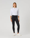 A woman modeling black high-waisted athletic leggings with a white long-sleeve polo shirt and white sneakers, standing against a light gray studio background.