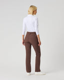 A woman with blonde hair is shown from the back wearing brown trousers, a white long-sleeve top, and white sneakers, standing against a light gray studio background.