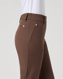 A side view of a person wearing brown tailored trousers and a white top against a plain light gray studio background.