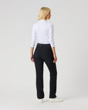 A woman with blonde hair is shown from behind wearing black trousers, a white long-sleeve top, and white sneakers, standing against a light gray studio background.