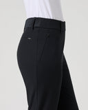 A side profile view of a person wearing black tailored trousers and a white top against a light gray studio background.