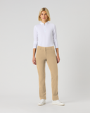 A woman stands against a light gray studio background wearing a white long-sleeve polo shirt, beige straight-leg trousers, and white sneakers.