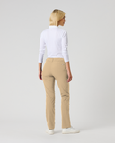 A woman with blonde hair is shown from behind wearing beige trousers, a white long-sleeve top, and white sneakers against a light gray studio background.
