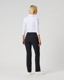 A woman with blonde hair is shown from behind wearing black slim-fit trousers, a white long-sleeve mock-neck top, and white sneakers, standing against a light gray studio background.