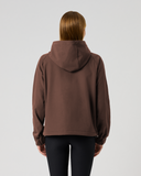 A person viewed from the back wearing a cropped brown hooded sweatshirt and black leggings against a plain light gray studio background.