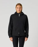 A woman modeling a black hooded zip-up jacket with front pockets, photographed against a plain light gray studio background.