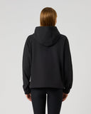 A model viewed from the back wearing a black hooded sweatshirt and black leggings against a plain light gray studio background.