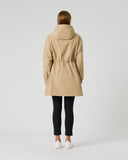A woman viewed from behind wearing a beige hooded trench coat with a drawstring waist, black leggings, and white sneakers, standing against a light gray studio background.