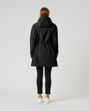 A model viewed from behind wearing a black hooded raincoat with a drawstring waist, black leggings, and white sneakers, set against a plain light gray studio background.