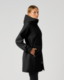 A woman modeling a black hooded jacket in a side profile view against a light gray studio background.