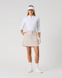 Daily Sports Stripe Bark Skort in warm camel and white vertical stripe print – women's pleated A-line golf skort with side pockets and tailored waistband, full length front view on model styled with white long sleeve polo and visor