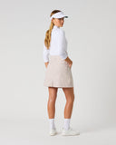 Daily Sports Stripe Bark Skort in warm camel and white vertical stripe print – women's pleated A-line golf skort showing pleated back panel and flared hem, three-quarter back view on model styled with white long sleeve polo and visor