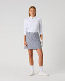 Daily Sports Stripe Dark Navy Skort in dark navy and white vertical pinstripe – women's pleated A-line golf skort with tailored waistband and side pockets, full length front view on model styled with white long sleeve polo and golf glove