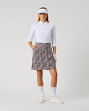 Daily Sports Dull Zebra Printed Skort in muted brown and white abstract zebra swirl print – women's A-line golf skort with side pockets and elasticated waistband, full length front view on model styled with white long sleeve polo and visor