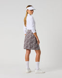 Daily Sports Dull Zebra Printed Skort in muted brown and white abstract zebra swirl print – women's A-line golf skort showing all-over print back panel and flared hem, three-quarter back view on model styled with white long sleeve polo and visor