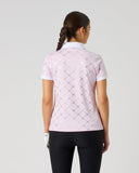 A woman viewed from behind wearing a light pink short-sleeve polo shirt with a subtle argyle pattern, paired with black pants, against a plain light gray studio background.