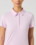 A woman wearing a light pink short-sleeve polo shirt, shown from the nose down against a plain light gray studio background.