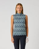A woman modeling a sleeveless mock-neck top with a blue, white, and gray wavy geometric pattern, paired with dark pants and a white glove, against a light gray studio background.