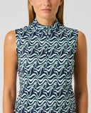 A woman wearing a sleeveless high-neck top with a navy blue and mint green wavy abstract pattern, shown against a plain light gray studio background.
