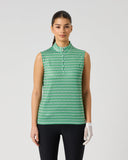 A model stands against a light gray studio background wearing a sleeveless collared button-front top with a green and white repeating geometric pattern, paired with black pants and a white glove.