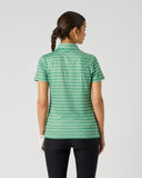 A woman viewed from the back wearing a short-sleeve collared shirt with a green and white geometric pattern, paired with black pants, against a plain light gray studio background.