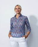 Woman wearing a patterned shirt and white pants against a plain background