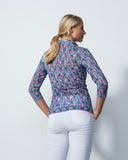 Woman wearing a patterned shirt and white pants against a plain background