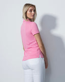 Woman wearing a pink polo shirt and white pants against a light gray background