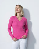 Woman wearing a pink sweater and white pants against a light gray background