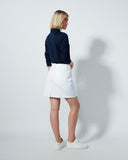 Woman wearing a navy sweater and white skirt against a plain background