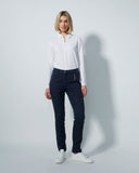 Woman wearing a white shirt and dark navy pants against a plain background