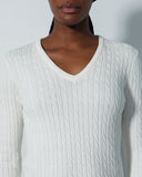 Person wearing a white cable knit sweater against a plain background