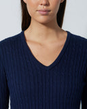 Woman wearing a navy blue cable knit sweater against a plain background