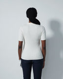 Person wearing a white ribbed sweater and dark pants against a light gray background