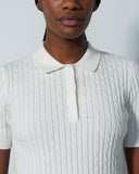 Person wearing a white ribbed knit shirt with a collar against a plain background