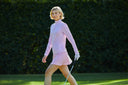 Woman in pink golf outfit walking on a golf course with a hedge in the background