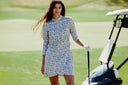 Woman in a floral dress standing on a golf course with a golf cart in the background.