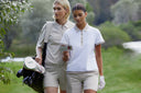 Two women walking on a golf course with golf bags and clubs.