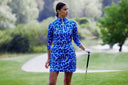 Woman in a blue patterned dress holding a golf club on a golf course