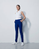 Woman wearing a white sleeveless top and blue pants against a white background