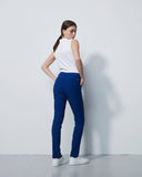 Woman wearing a white top and blue pants against a plain background