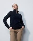 Woman wearing a dark blue sweater and beige pants against a light gray background