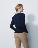 Woman wearing a navy sweater and beige pants against a white wall