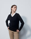 Woman wearing a black sweater over a white shirt with beige pants on a light gray background