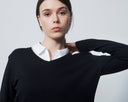 Woman wearing a black sweater over a white shirt on a plain background