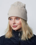 Person wearing a beige knit beanie and black jacket against a light gray background