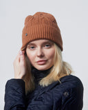 Woman wearing a brown knit beanie and dark jacket on a light background